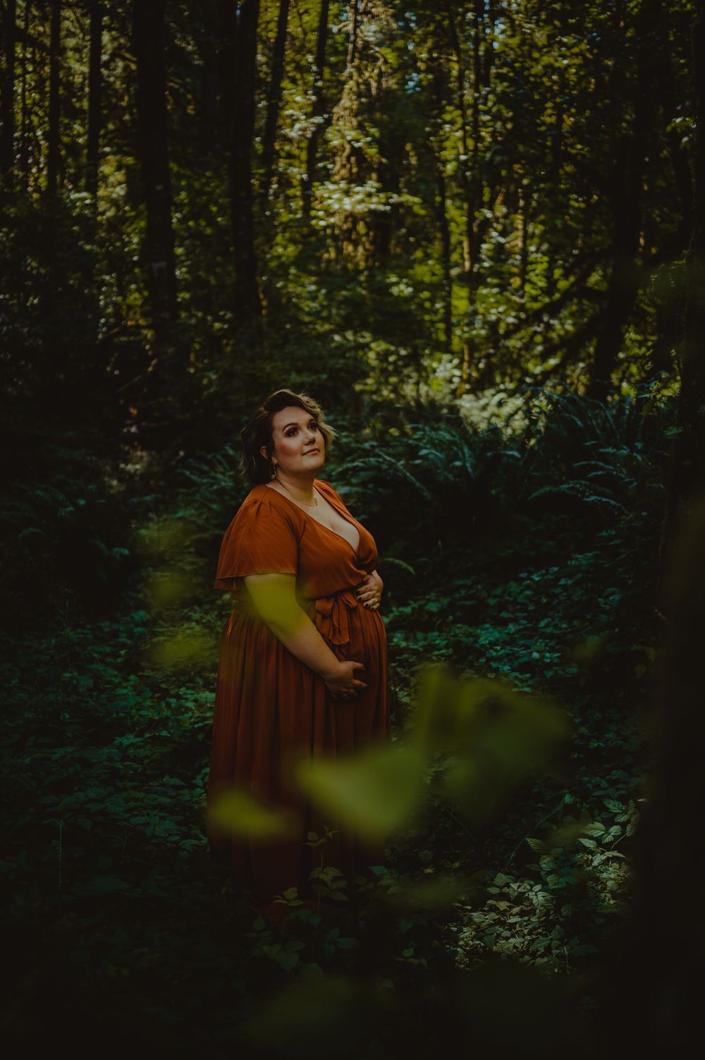 Artistic forest photoshoot featuring someone in a flowing rust-colored dress among dark trees.