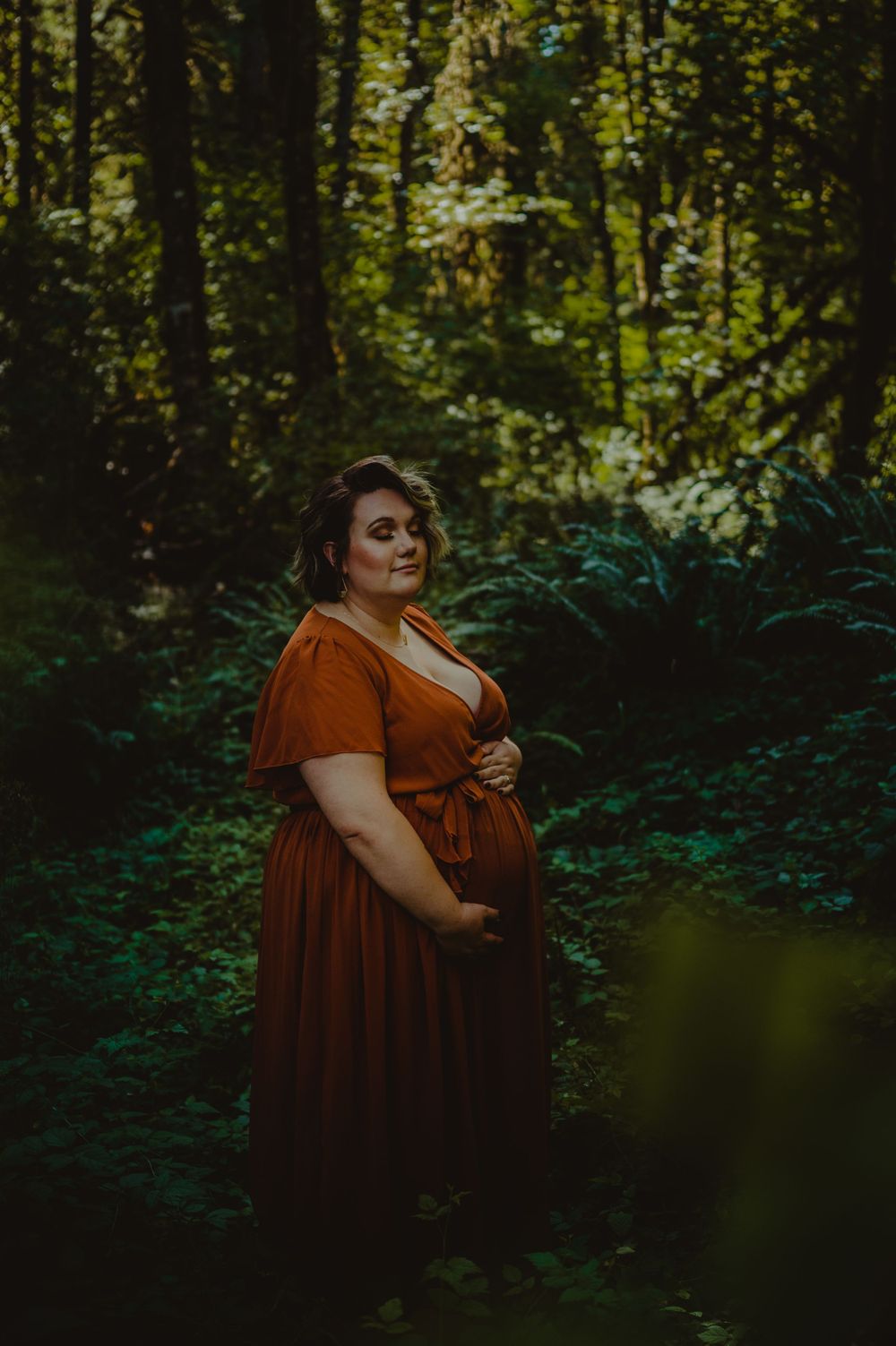 Moody forest photography featuring a rust-colored dress among lush greenery.