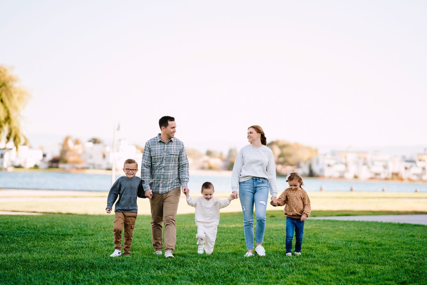 A beautiful family walking together on green grass near waterfront during golden hour sunset.