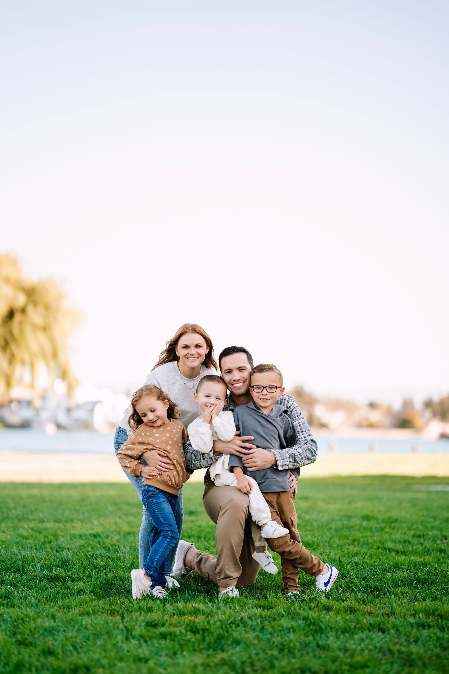 A family group poses together on green grass near a waterfront with weeping willows in the background.
