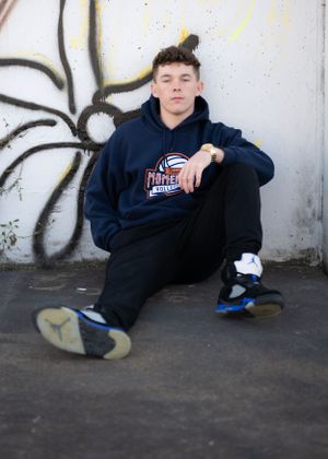 Casual portrait of someone sitting against graffiti wall wearing navy hoodie and sneakers.