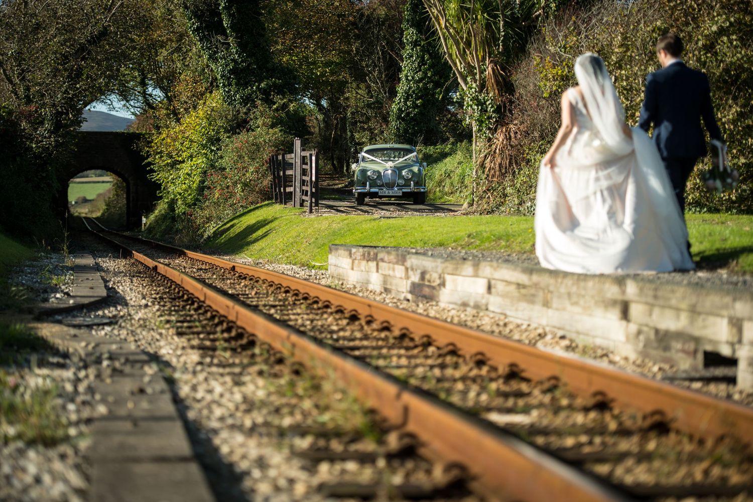 Bride and Groom walk to their Jaguar alongside a railway line to London