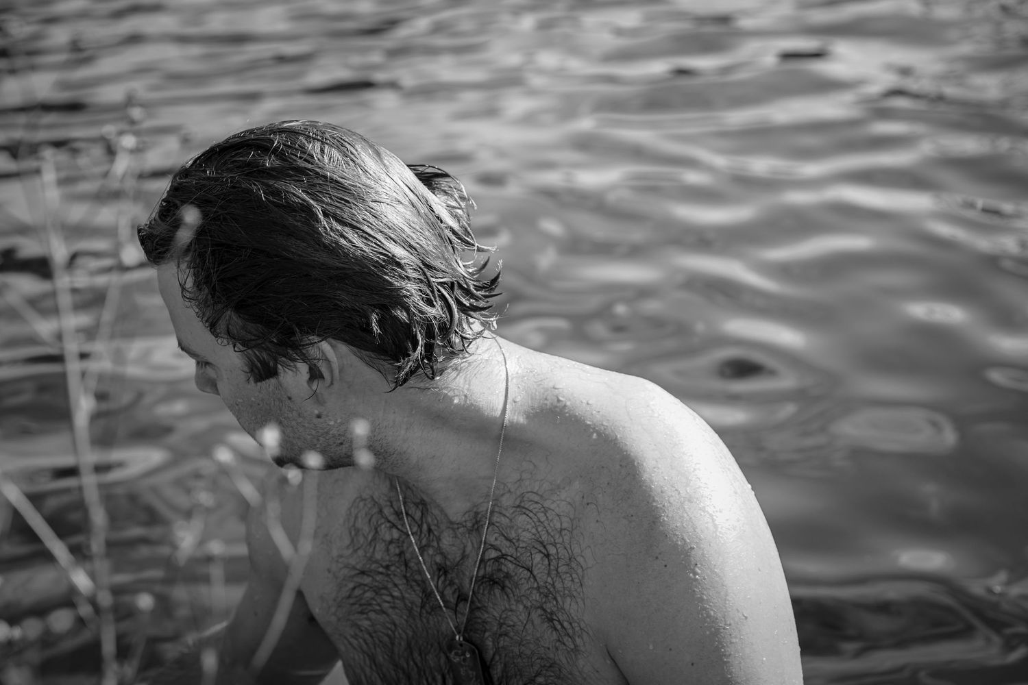 A person soaks in rippling water, shown from behind in dramatic black and white photography.