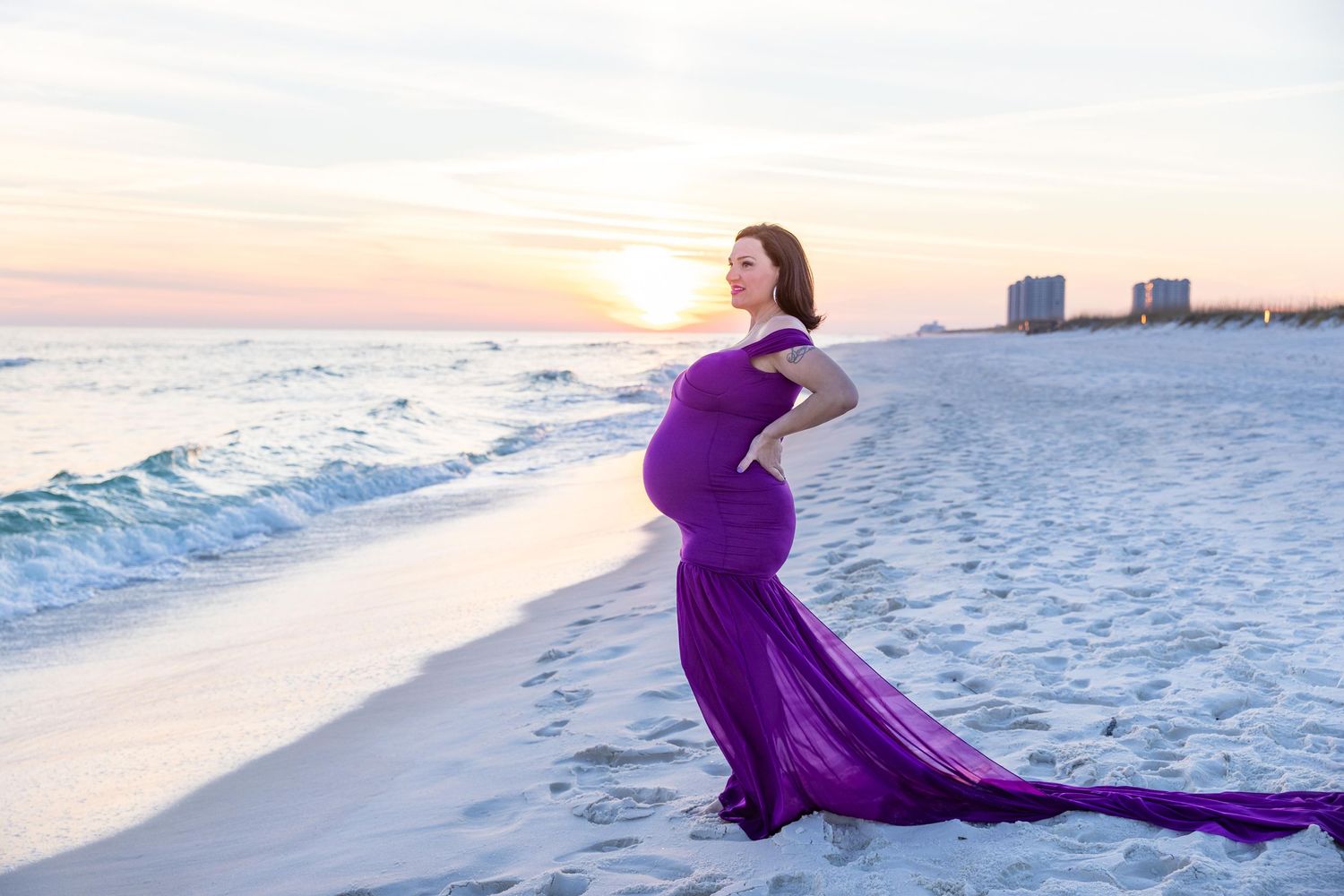 Maternity beach portrait featuring woman in purple gown during golden sunset.