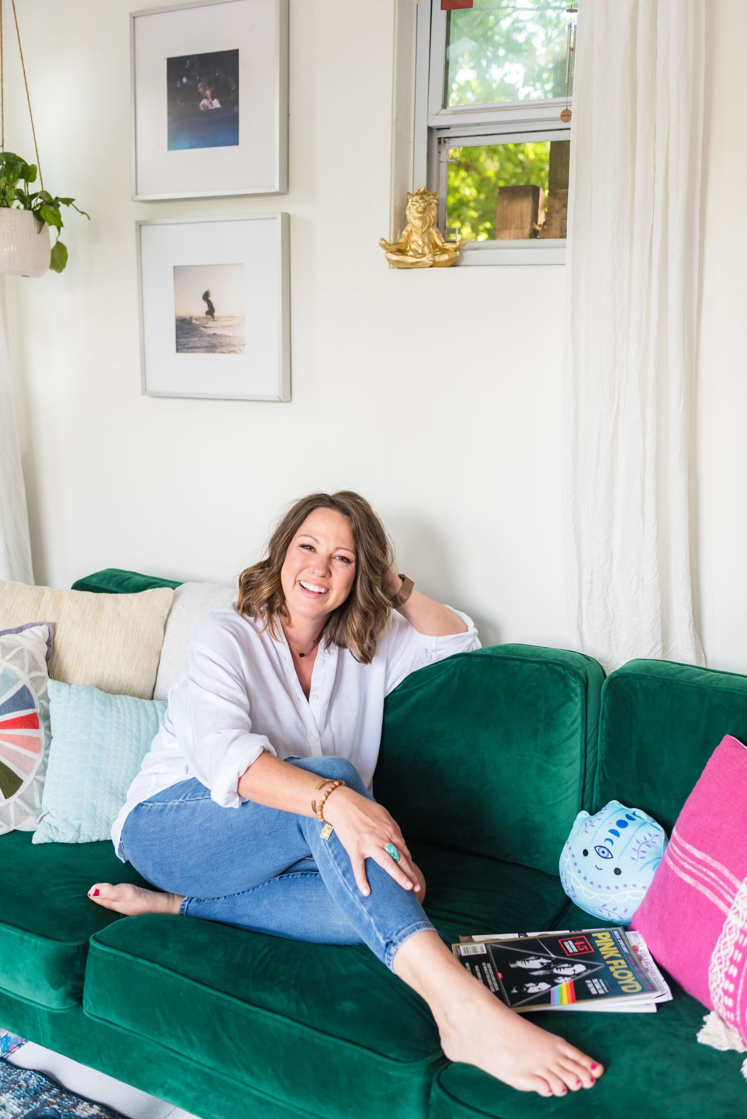 Relaxed reading moment on emerald green velvet couch with decorative pillows and framed art.