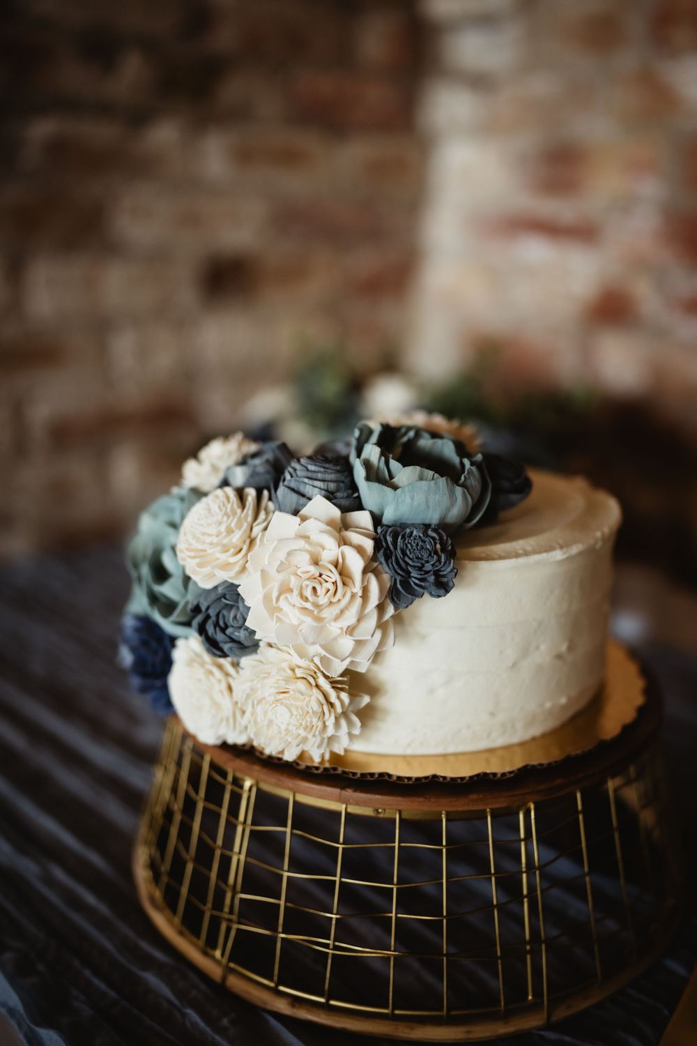 Elegant white wedding cake decorated with dusty blue and cream sola wood flowers on a gold geometric stand.