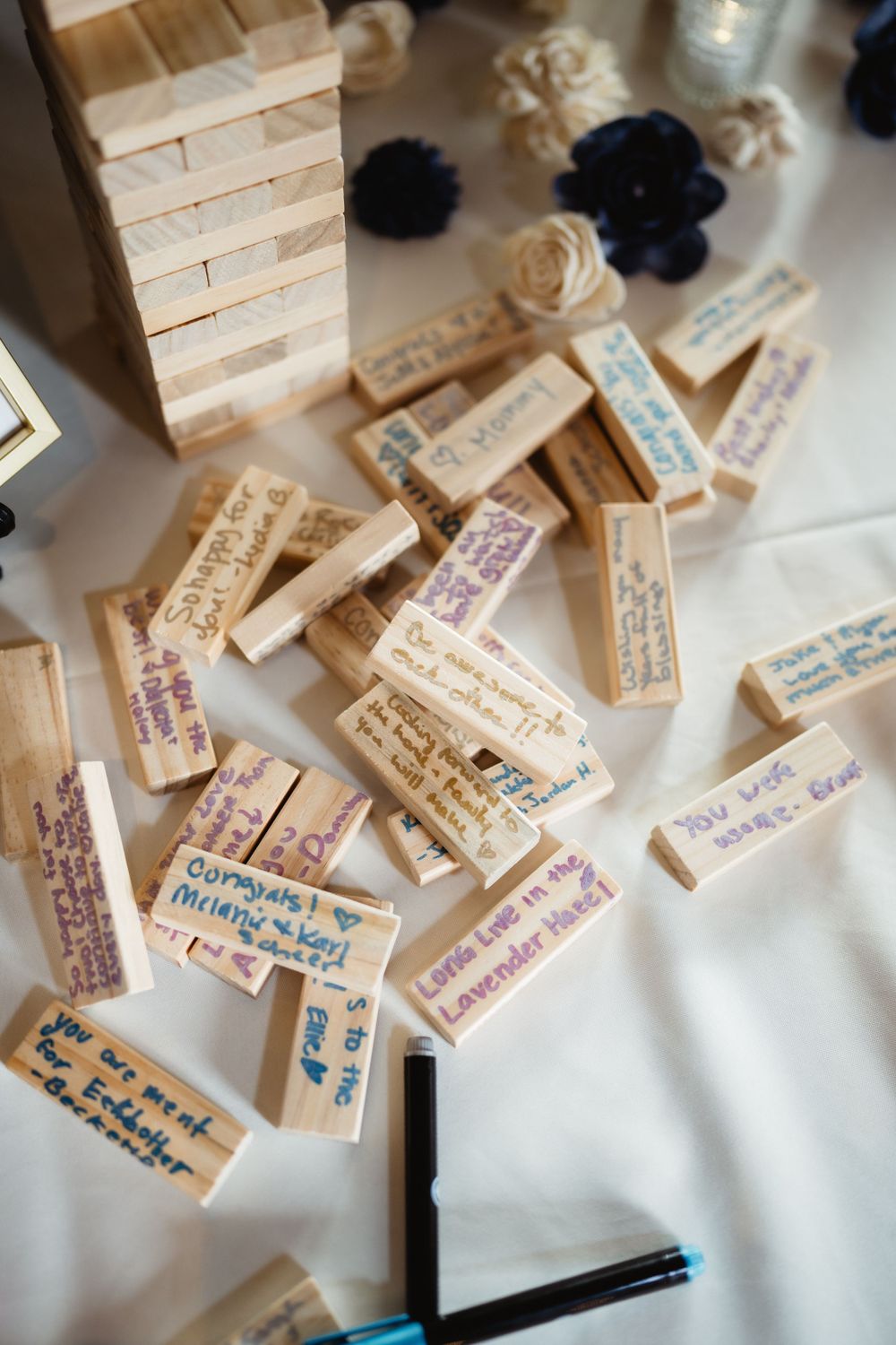Wooden Jenga blocks with handwritten messages spread across white tablecloth as wedding guest book alternative.