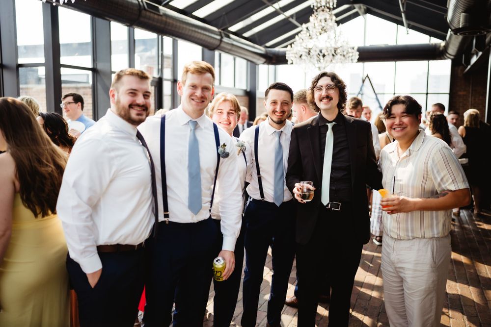 A group of formally dressed guests gather at an indoor reception venue with a chandelier.