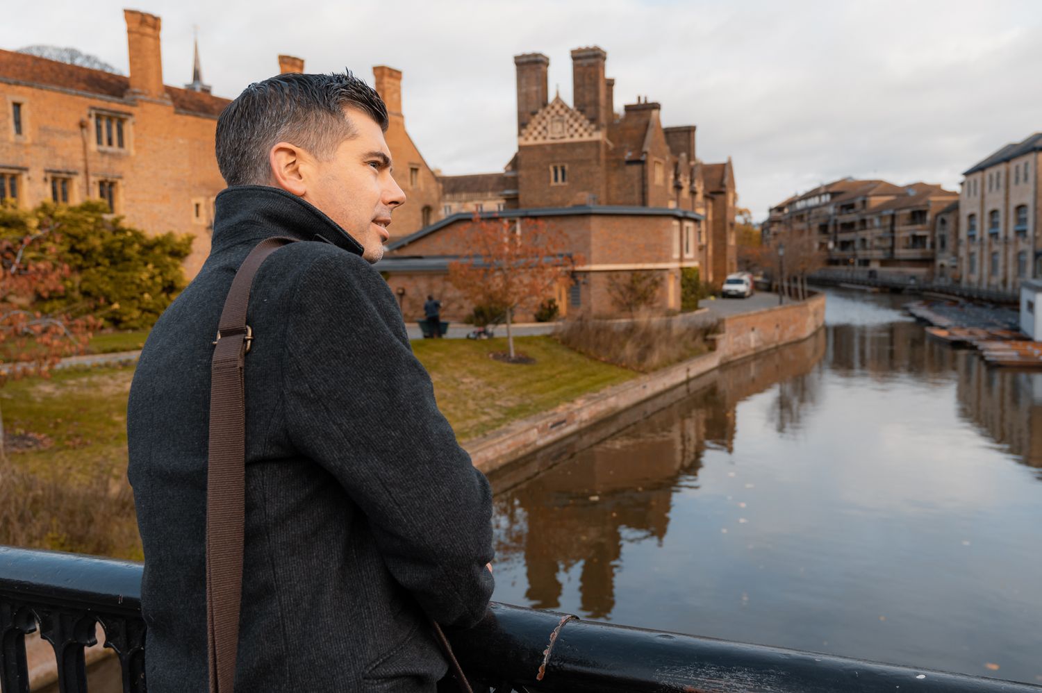 founder man standing on bridge with coat and bag looking over a river