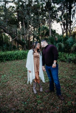 A romantic couple poses in a mossy forest setting with Spanish moss and palm fronds in the background.