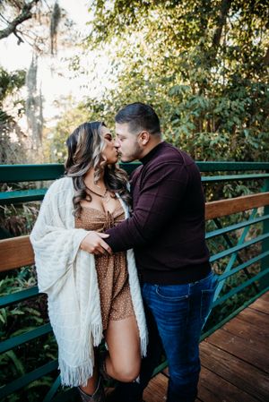 An intimate moment between a couple on a wooden bridge with sunlight filtering through trees.