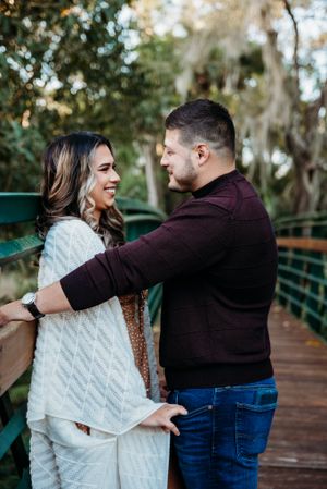 A couple shares a joyful moment on a wooden bridge surrounded by lush greenery.