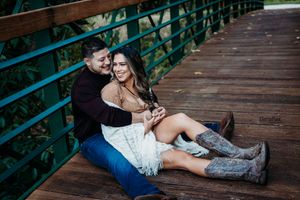 A couple sits together on a wooden boardwalk with teal railings in a natural setting.