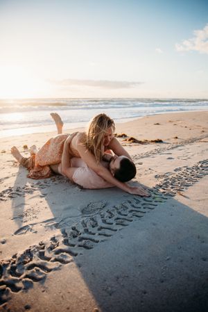 A romantic beach moment captured from above as a couple lies in the sand at sunset.