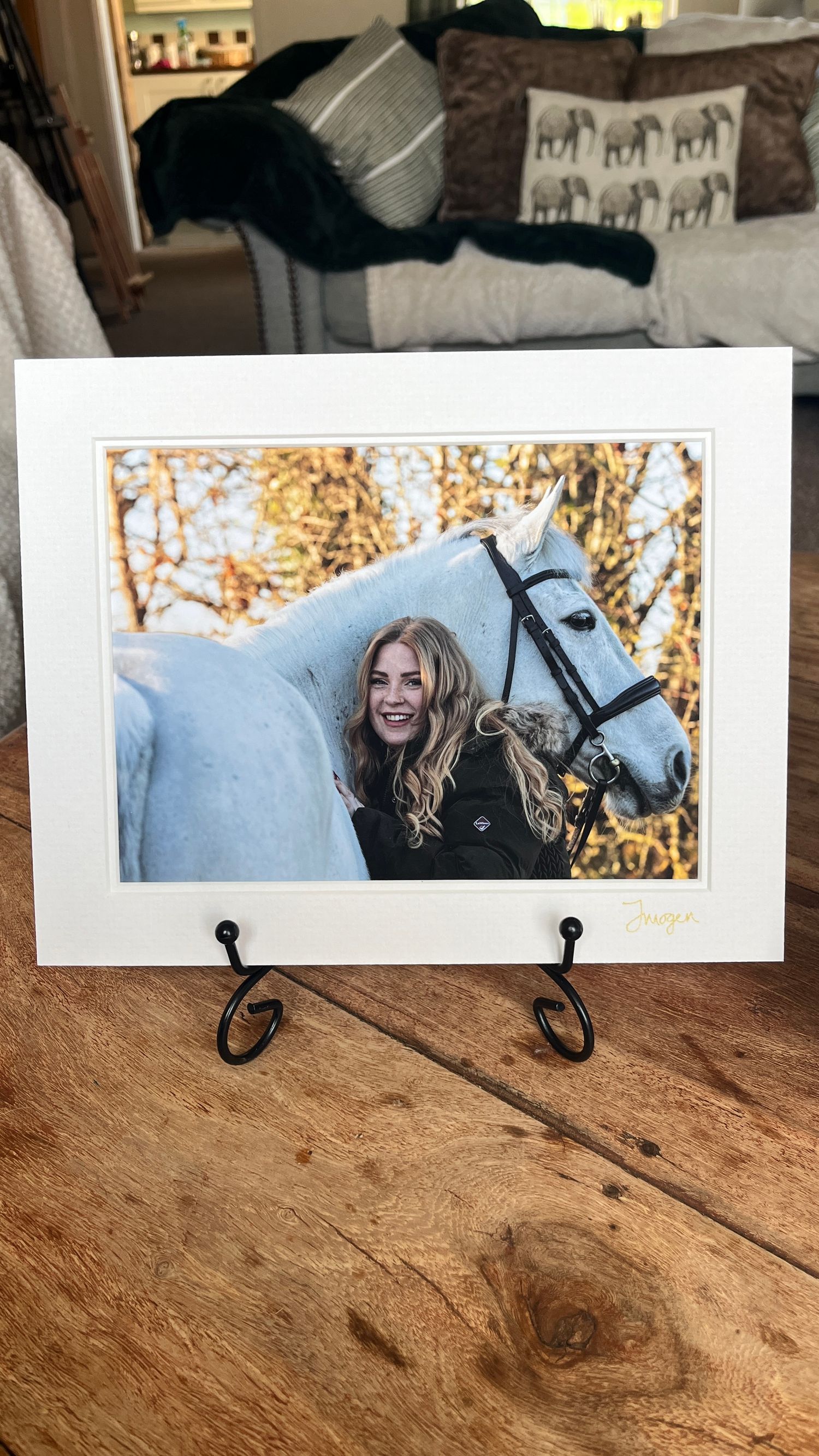 A framed photograph of someone with a white horse sits on display with a cat in the background.