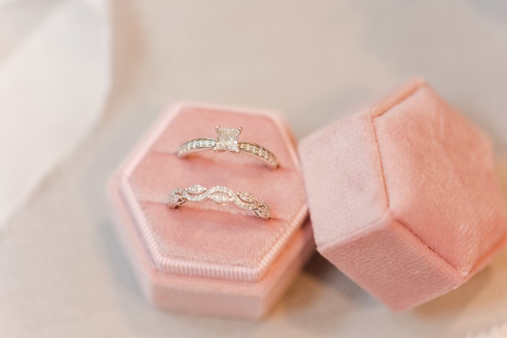 Two delicate diamond rings nestled in blush pink velvet hexagonal ring boxes.
