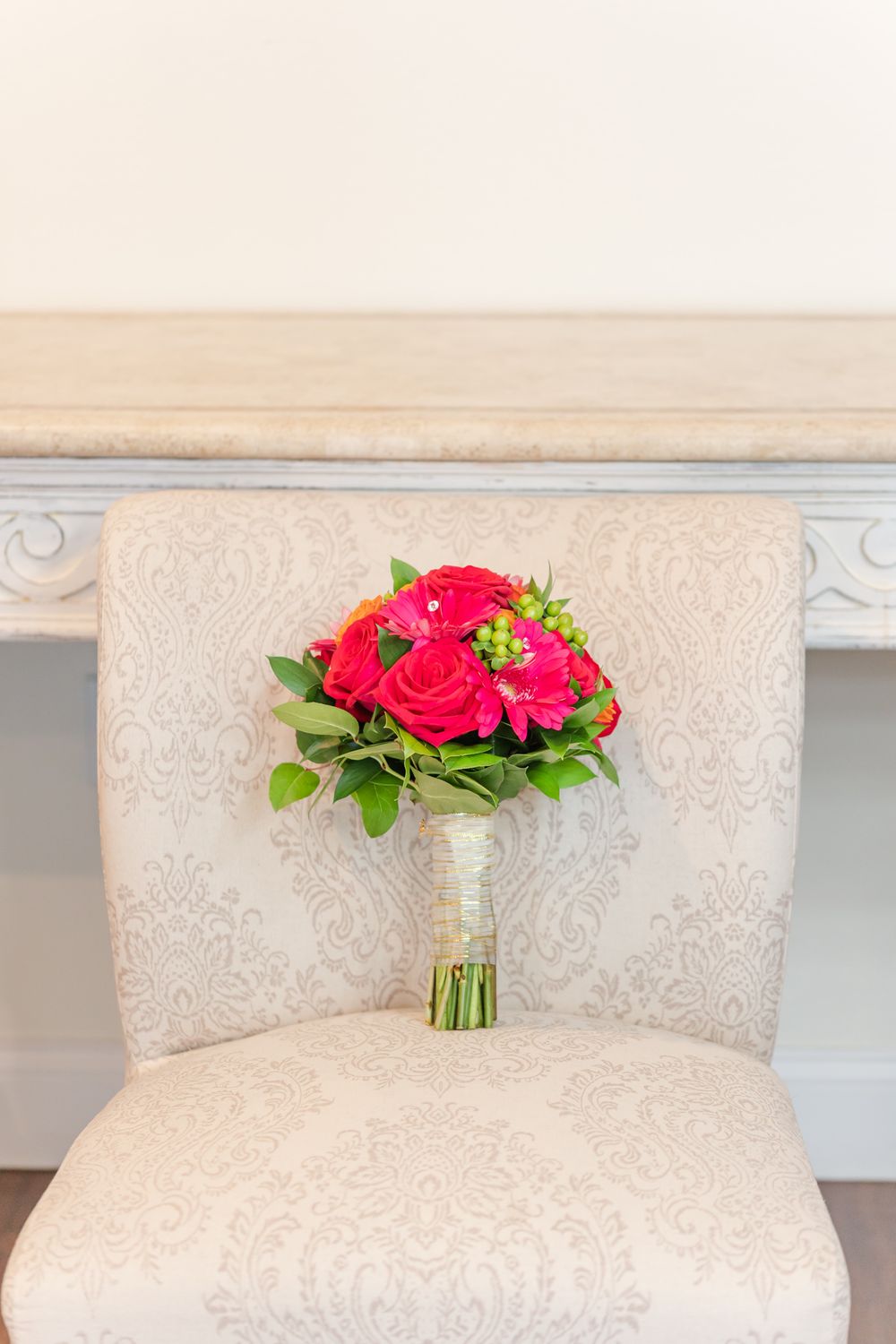 Vibrant red rose wedding bouquet resting on a cream damask upholstered chair.