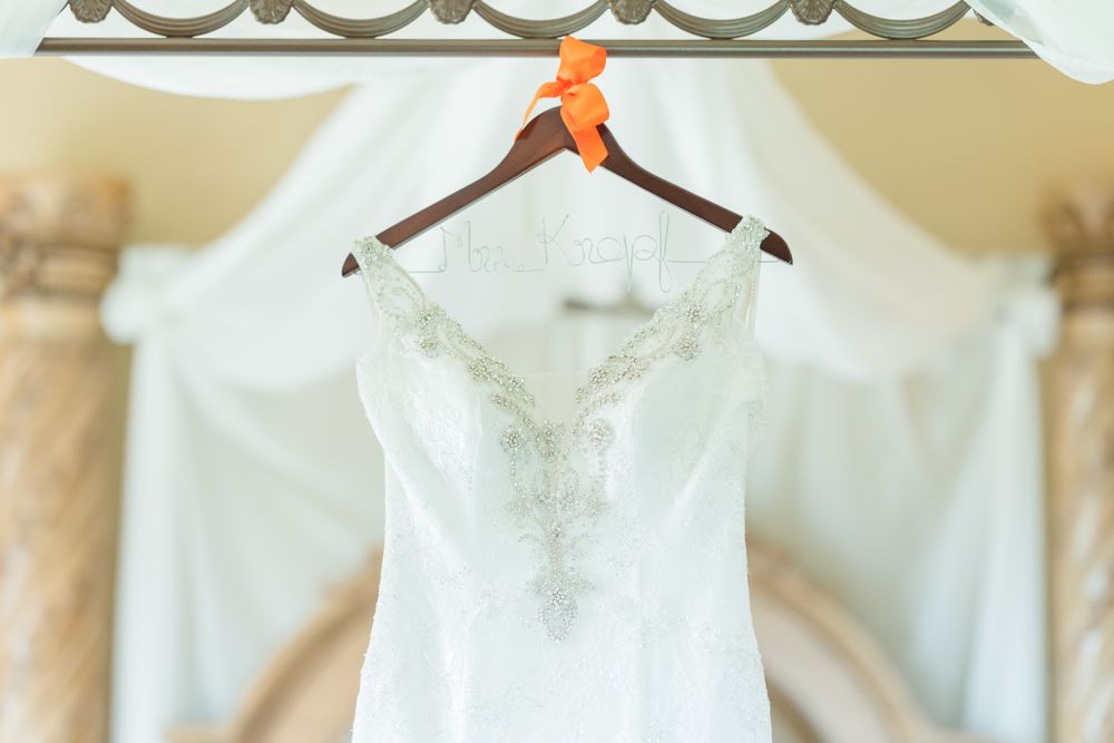 Elegant white wedding gown hanging on wooden hanger against light backdrop.