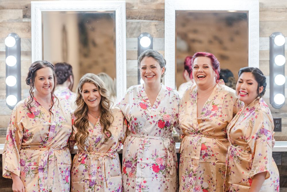 Wedding party in matching floral robes pose together smiling.