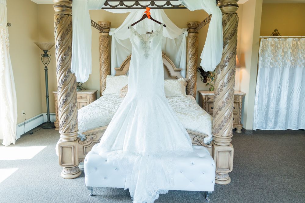 A white wedding dress displayed on an elegant four-post bed with ornate columns.