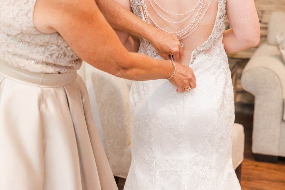 Close-up of hands adjusting the back buttons of a white lace wedding dress.