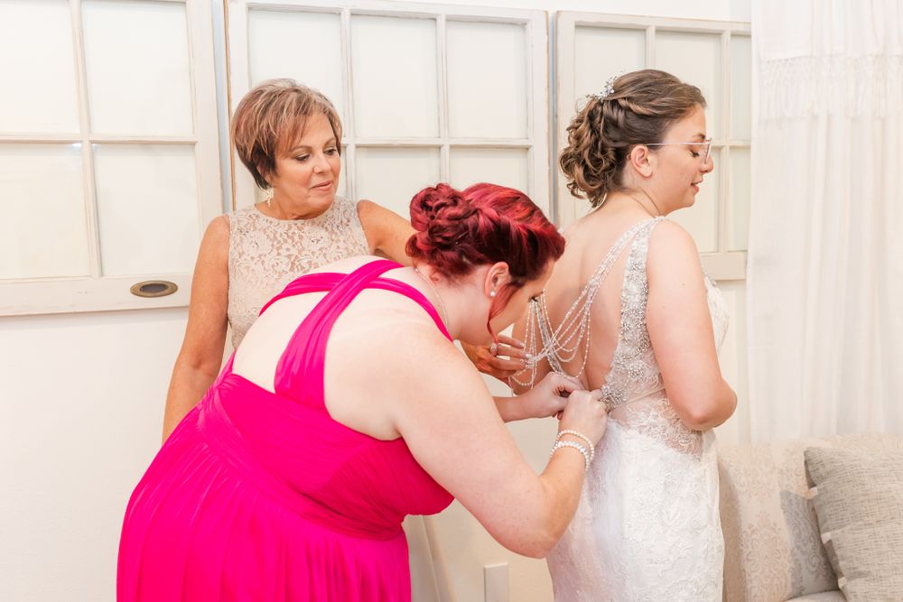 Wedding party helping with final dress adjustments in a bridal preparation room.