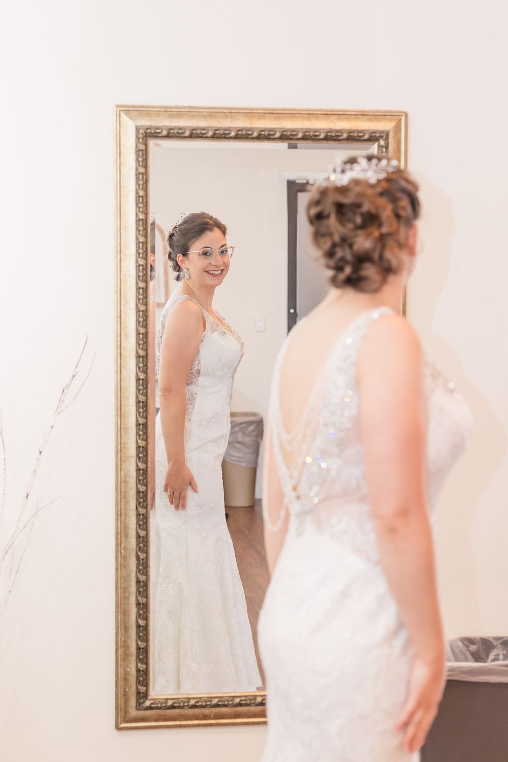 Reflection of a wedding dress being admired in an ornate gold-framed mirror.