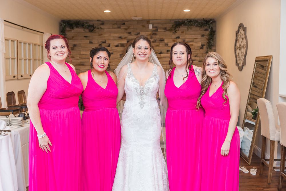 Wedding party posing together in bright pink dresses and a white bridal gown.