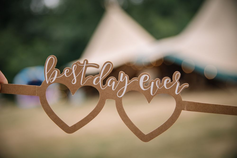 Wooden 'best day ever' wedding decor with heart cutouts against blurred outdoor background.