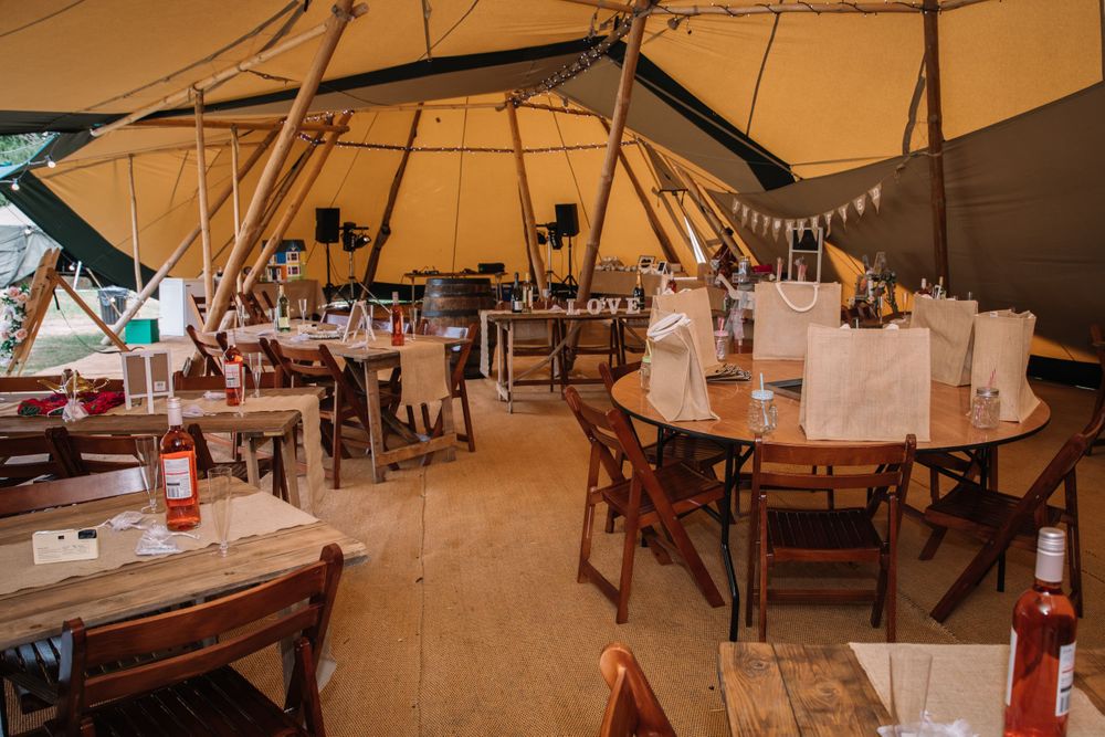 Interior of a rustic tipi tent wedding venue with wooden tables and chairs set up for dining.