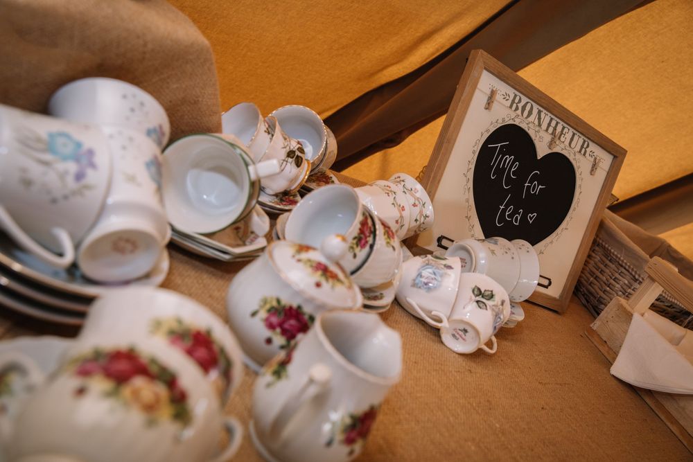 Vintage teacups with floral patterns and a small chalkboard sign displayed at a wedding.