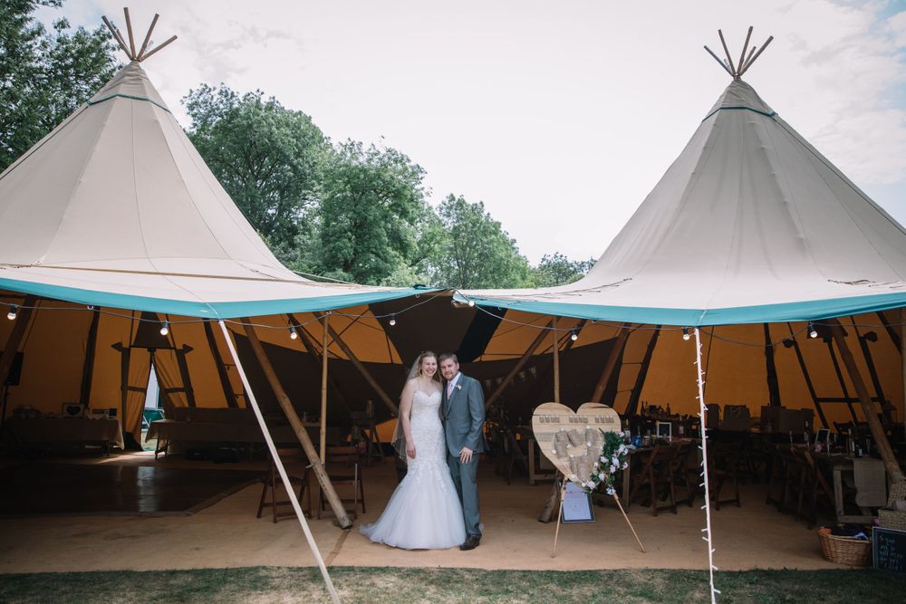 Two white tipi tents set up in a grassy field for an outdoor event.