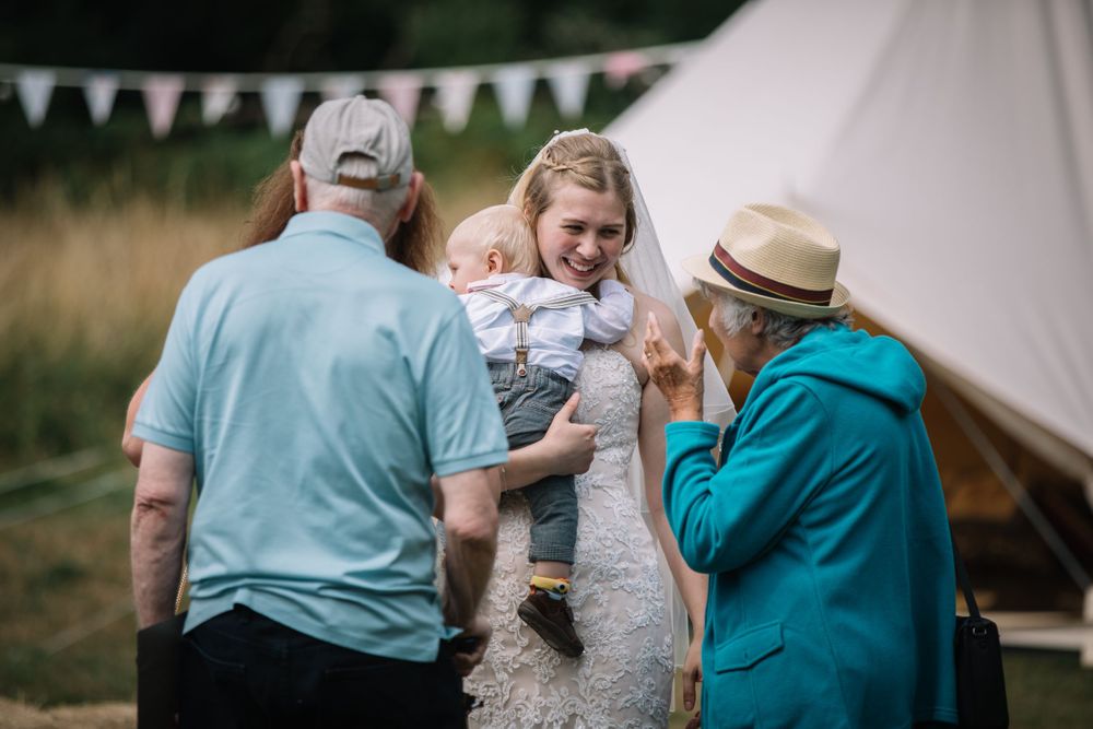 Small group gathering outside a white tent at an outdoor celebration.