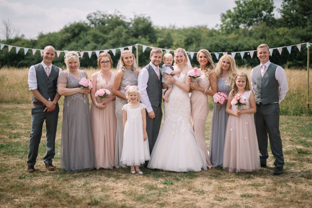Wedding party in neutral tones poses together on a grassy field with white bunting decorations.