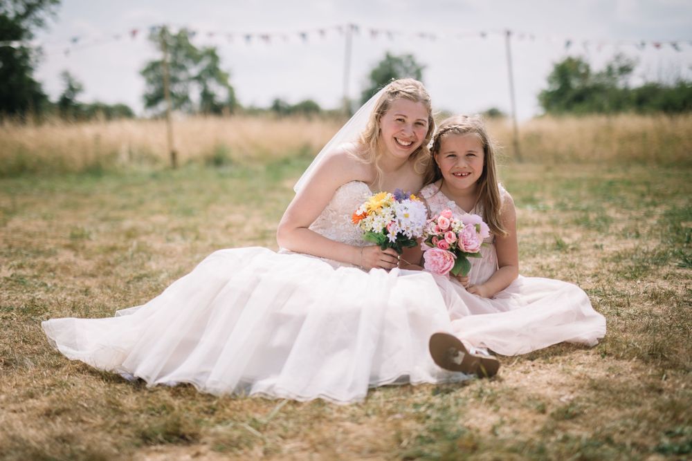 White wedding dress spreads across dried grass field with bunting flags in background.