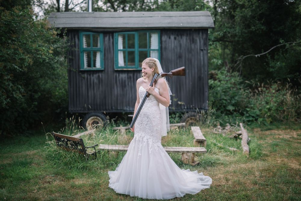 A bride in a lace wedding dress stands in front of a rustic wooden cabin.