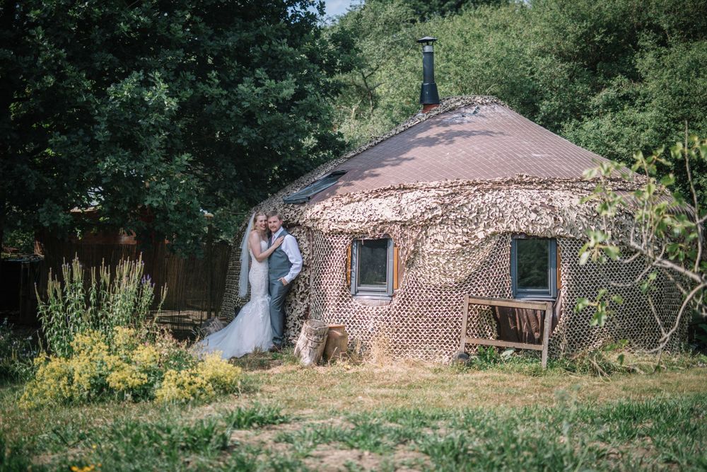 Newlyweds pose outside a round brick building with green surroundings.