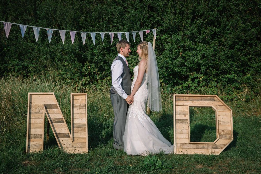 Romantic wedding portrait with couple standing between large wooden N and D letters outdoors.
