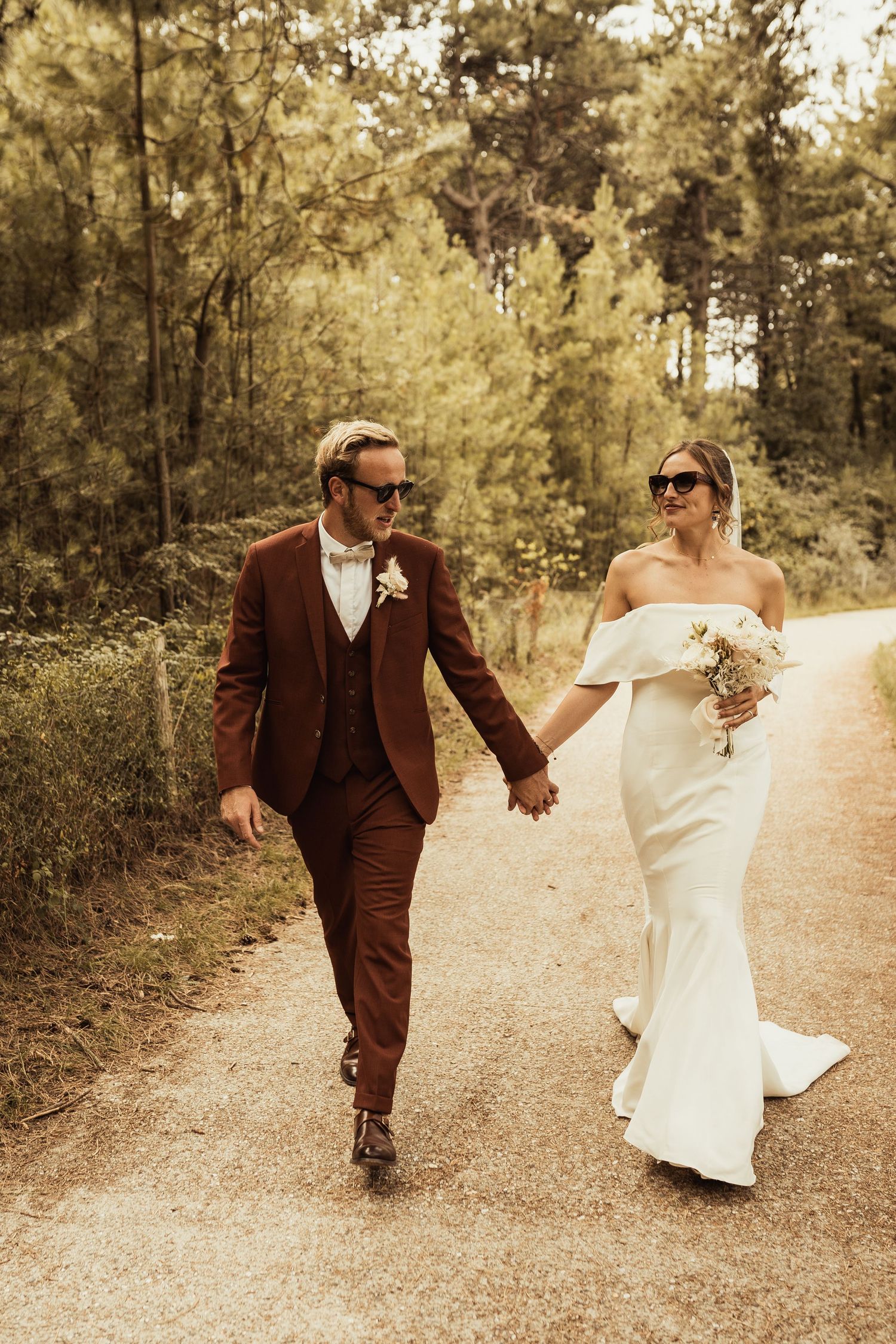 Couple walking hand in hand on forest path in formal wedding attire.
