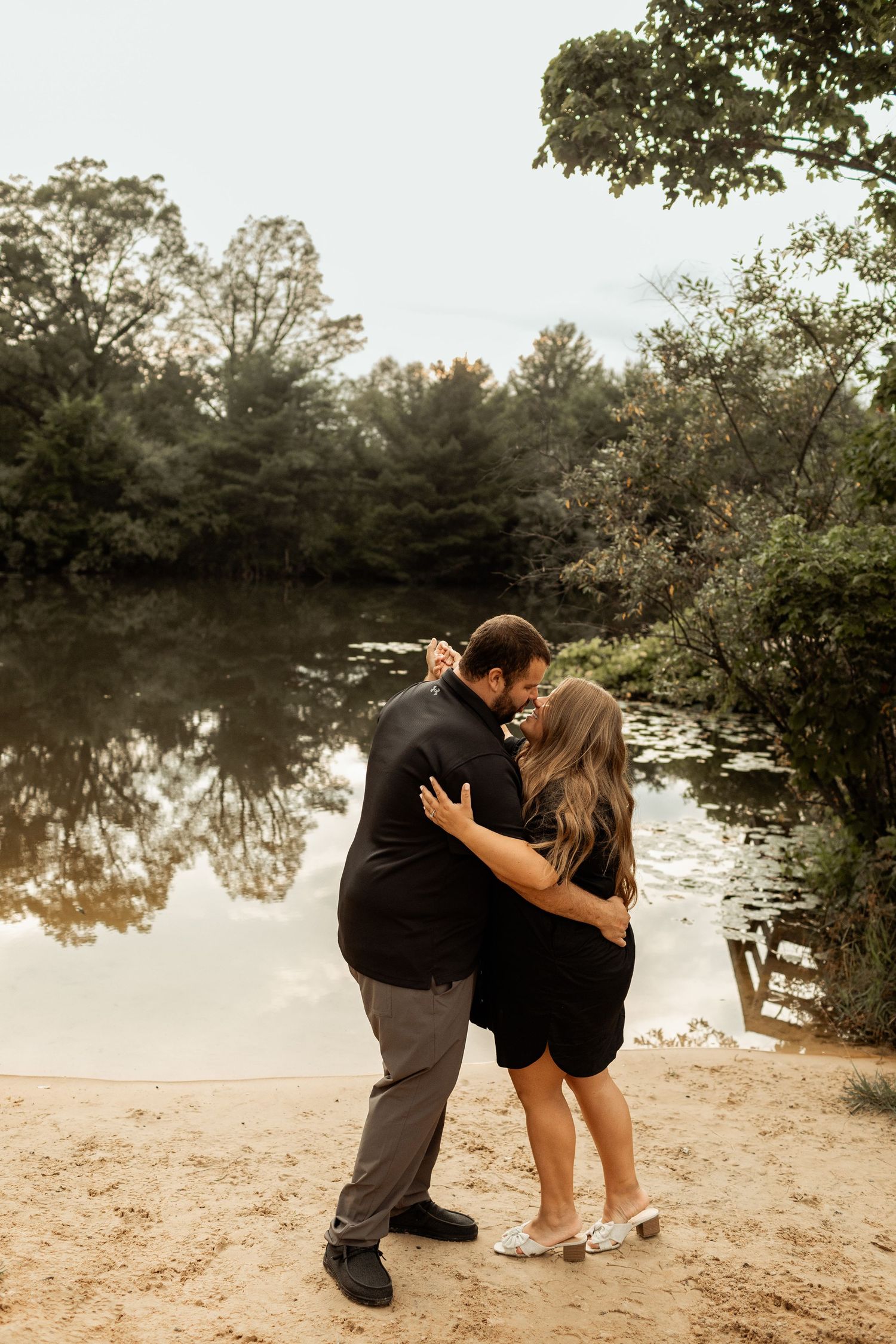 A romantic moment between a couple embracing by a serene pond at sunset.