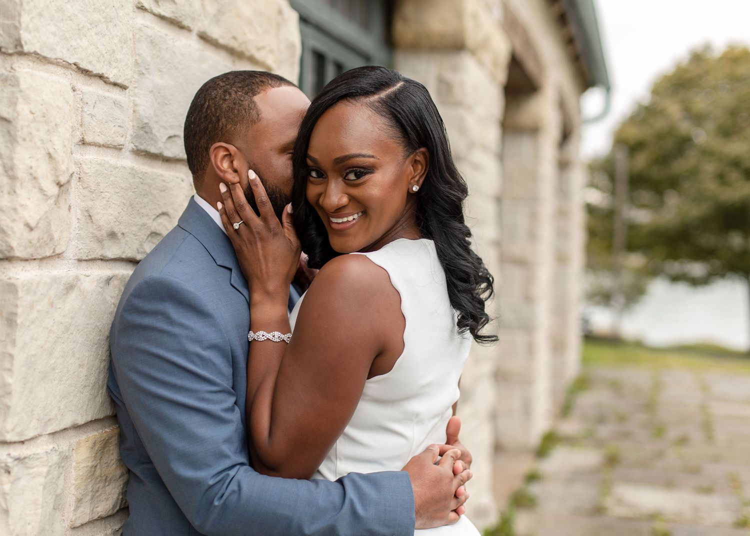 A joyful couple shares a tender moment against a stone wall backdrop.