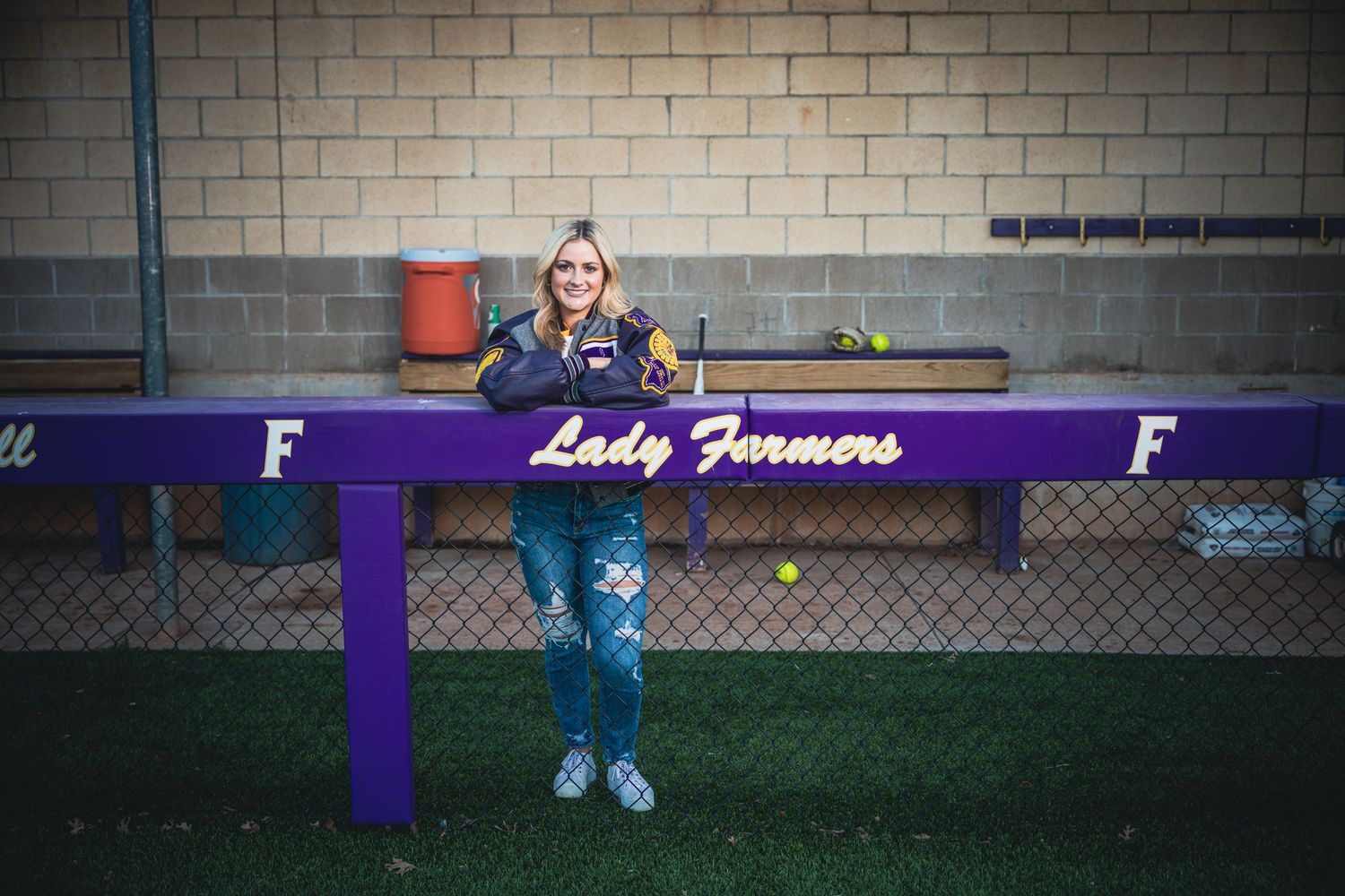 Purple dugout bench with 'Lady Farmers' text at a softball field.