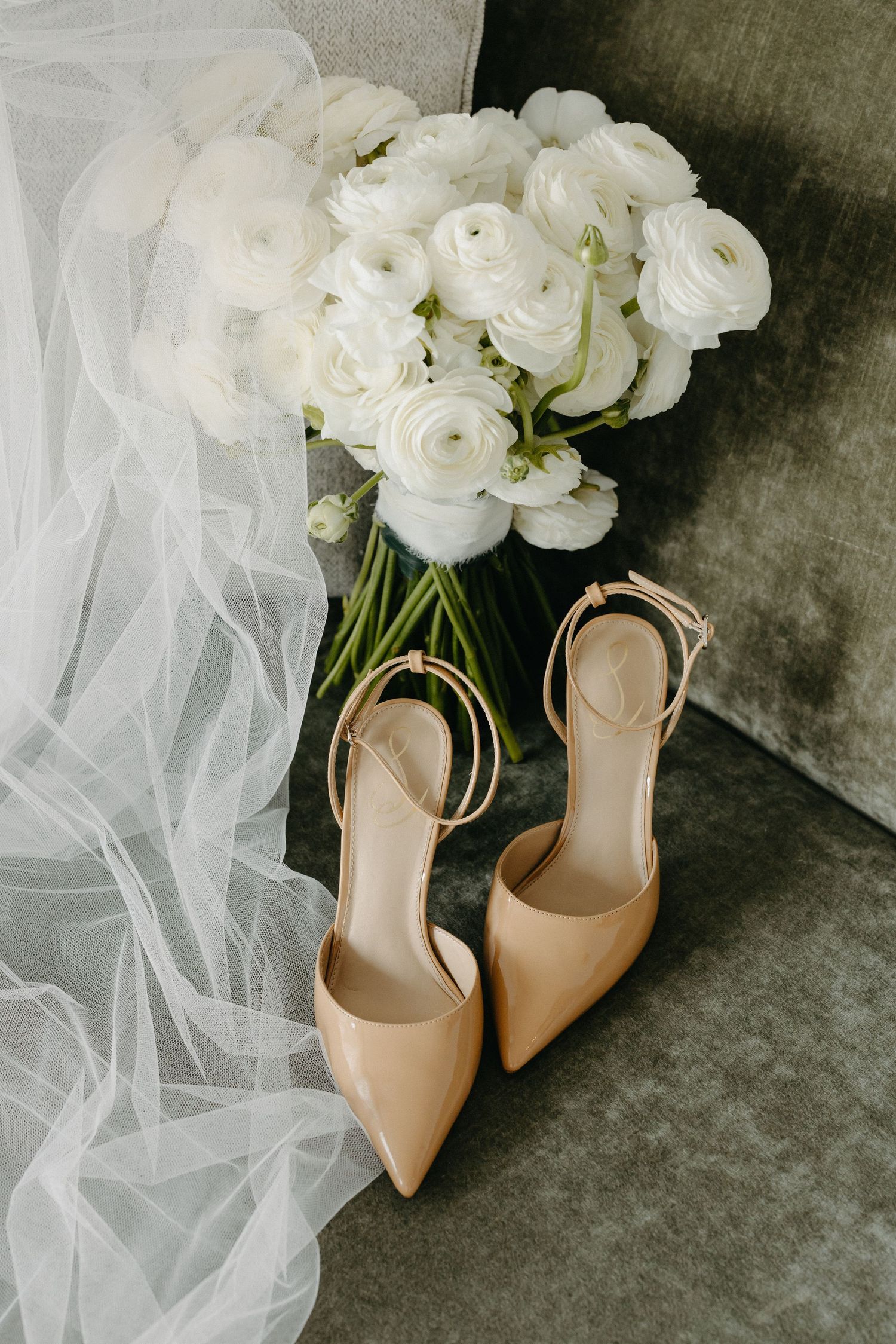 Elegant nude leather bridal heels paired with white roses and flowing tulle veil on grey background.