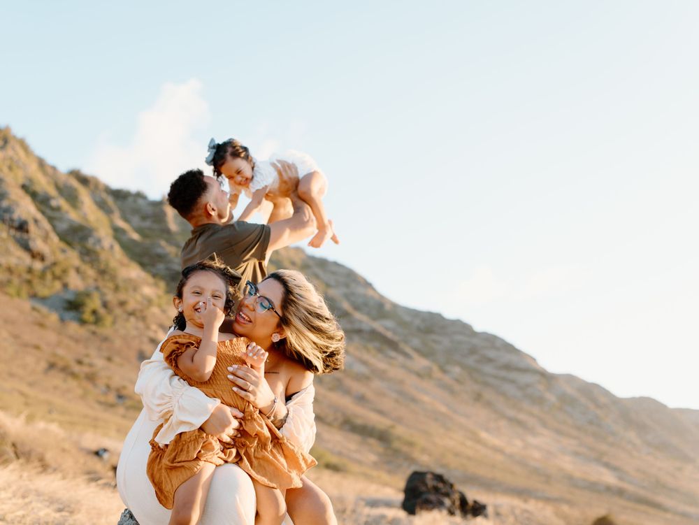A family photoshoot by Moments With Kell with a mountain backdrop on Oahu in Hawaii with parents and laughing children