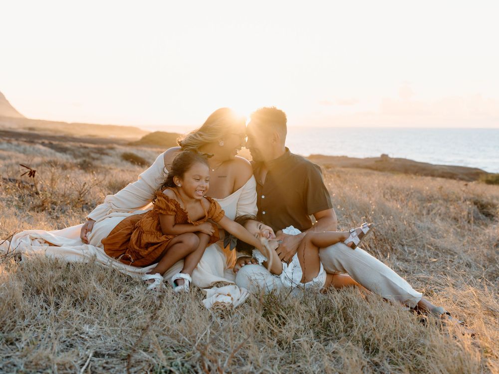 A family photoshoot by Moments With Kell with a sunset backdrop on Oahu in Hawaii with parents and children sitting