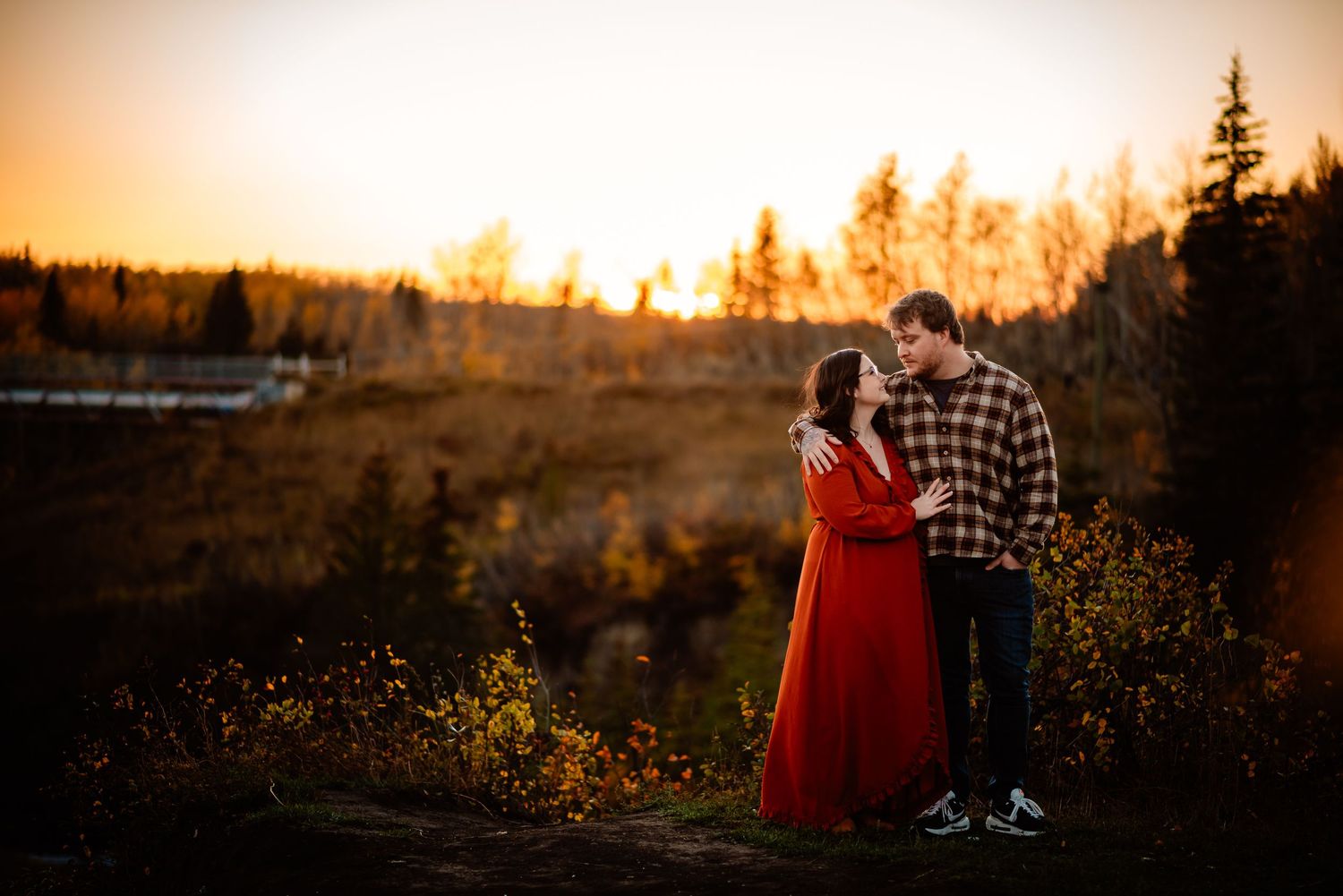 Couple stands together against golden sunset in rustic outdoor setting.