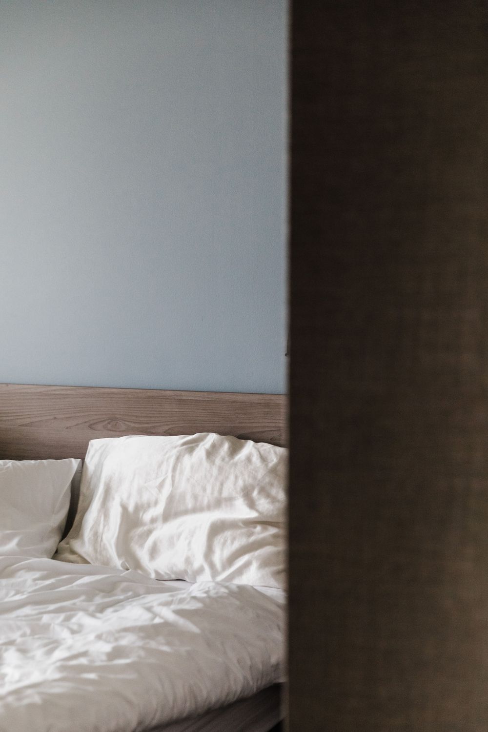 Minimalist bedroom interior with unmade white bedding and neutral walls viewed through a doorframe.