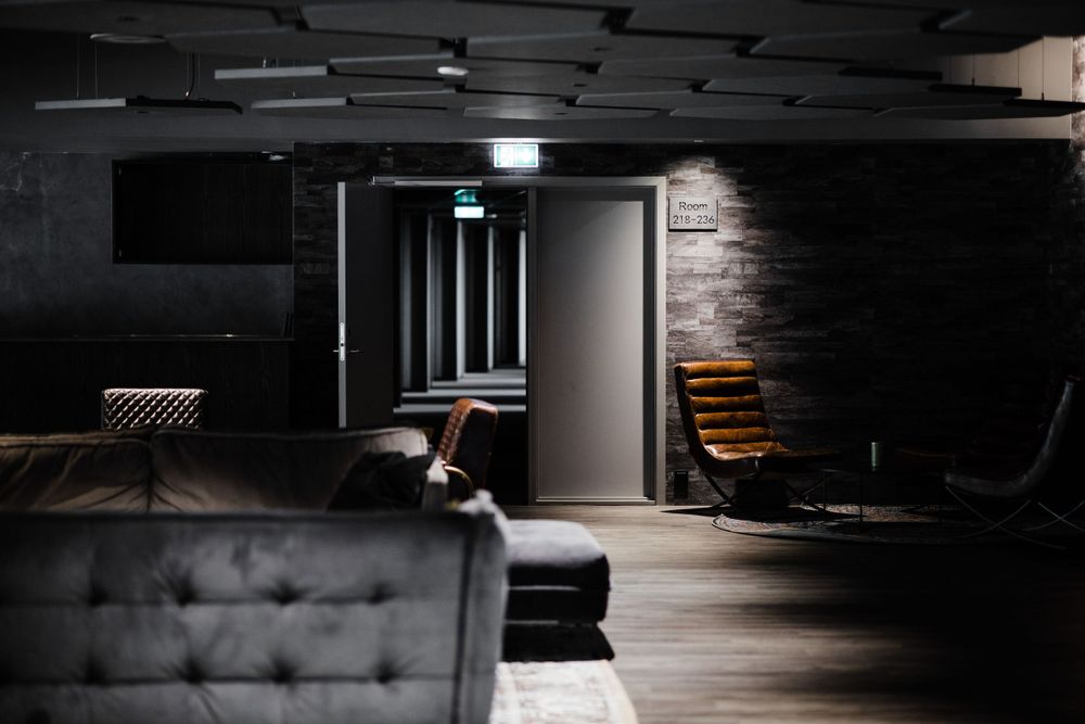 Modern dark lounge area with leather couches and moody lighting featuring an illuminated doorway.