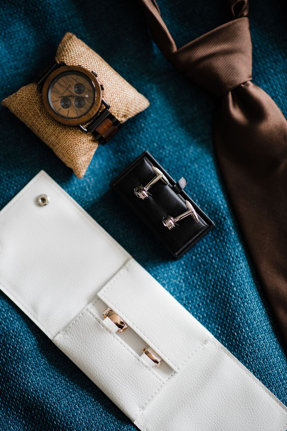 Groom's accessories including watch, cufflinks and tie arranged on blue fabric.