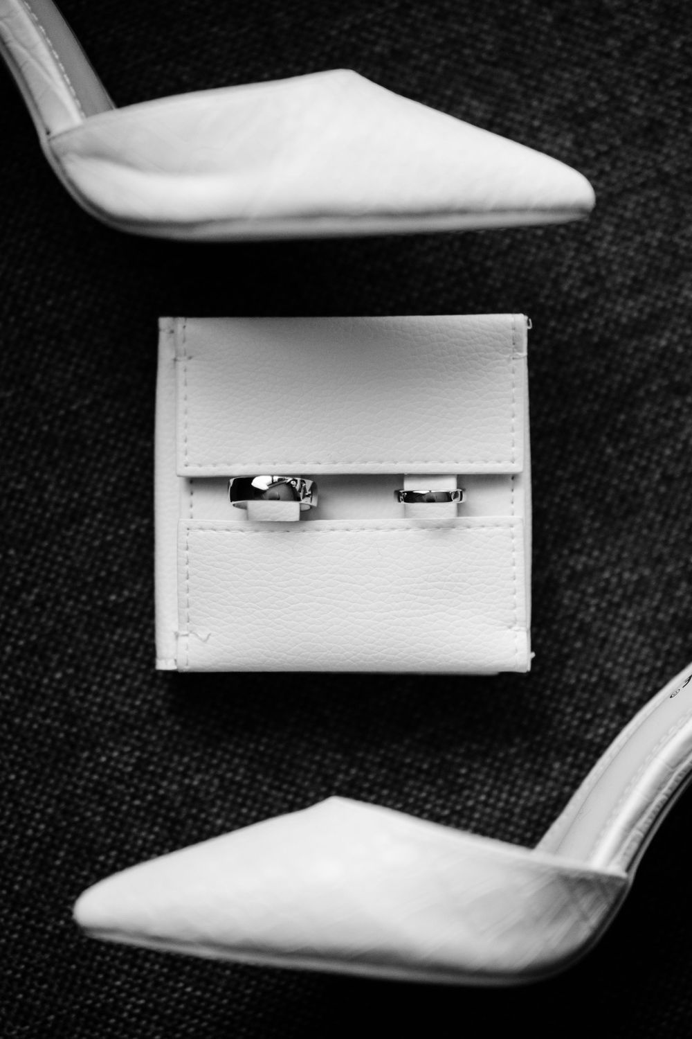 Wedding rings in a white box surrounded by elegant white heels on dark fabric.